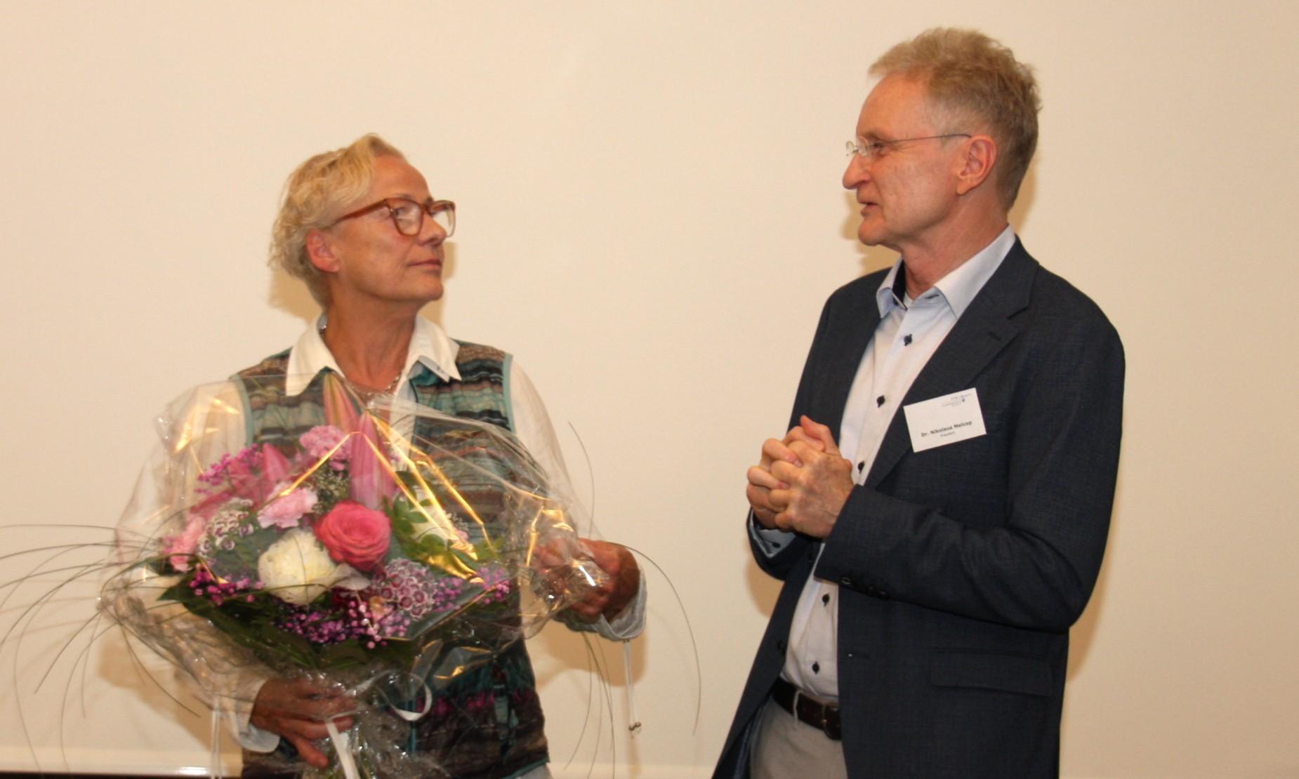 Eine Frau hält einen großen Blumenstrauß in der Hand, den sie von dem nebenstehenden Mann überreicht bekommen hat.